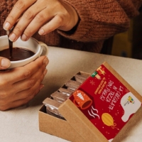 Preparato per cioccolata calda nella confezione natalizia, accanto al preparato in tazza pronto da consumare
