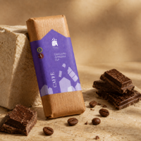 Cioccolato di modica Don Puglisi al caffè, tavoletta incartata poggiata su un supporto circondata da chicchi di caffè e pezzi di cioccolato